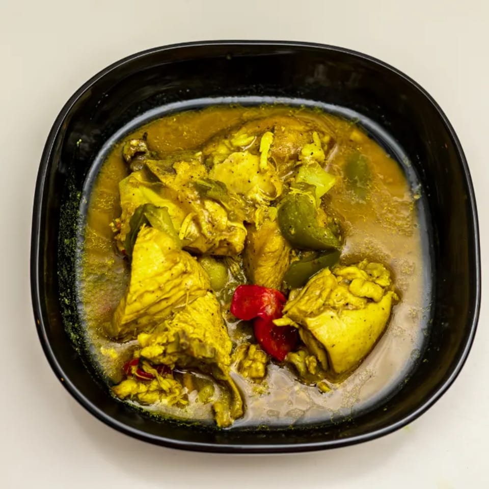 CaribeExpress's vibrant yellow Caribbean chicken curry with green and red peppers in a black bowl.