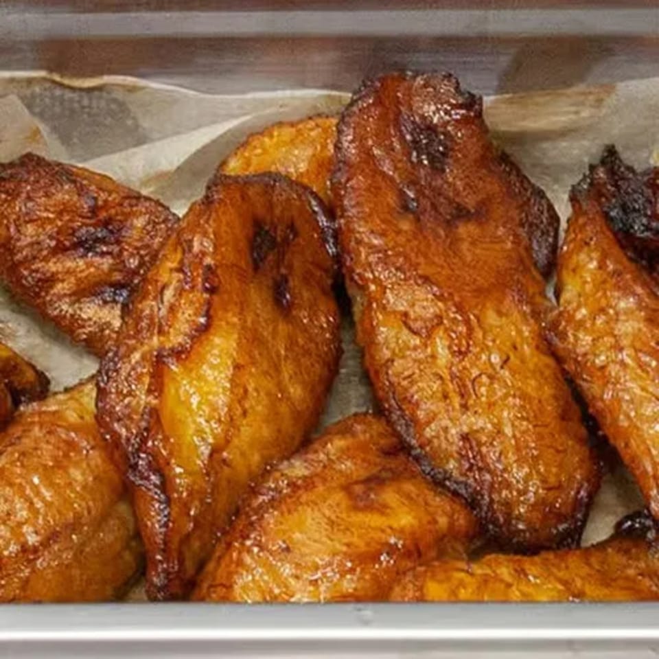 Close-up of several golden-brown fried plantains, glistening with oil, in a metal tray lined with parchment paper.