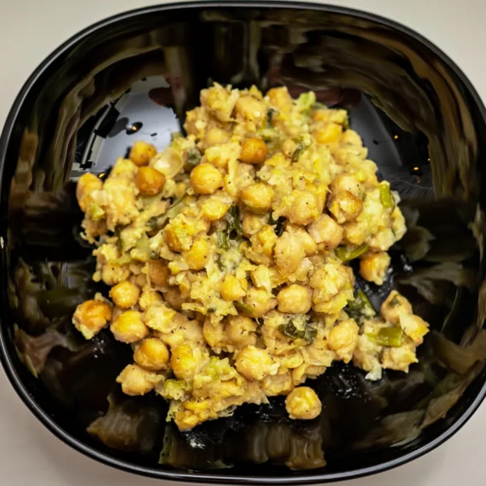 A black bowl filled with a Caribbean chickpea dish, featuring yellow chickpeas and green vegetables.